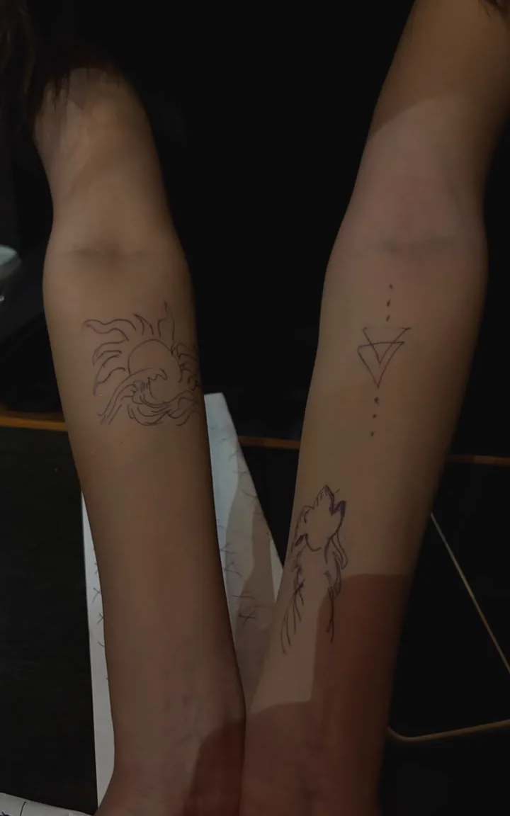 Two forearms held together, each covered with temporary drawings.