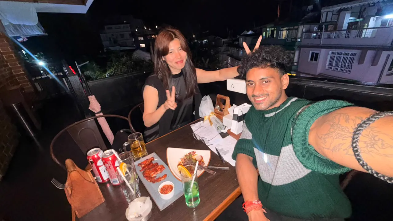 Saharsh and Sonam taking a wide selfie at the cafe with food and drinks on the table.