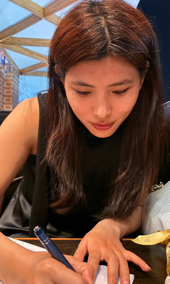 Sonam writing or drawing on paper at the restaurant table.