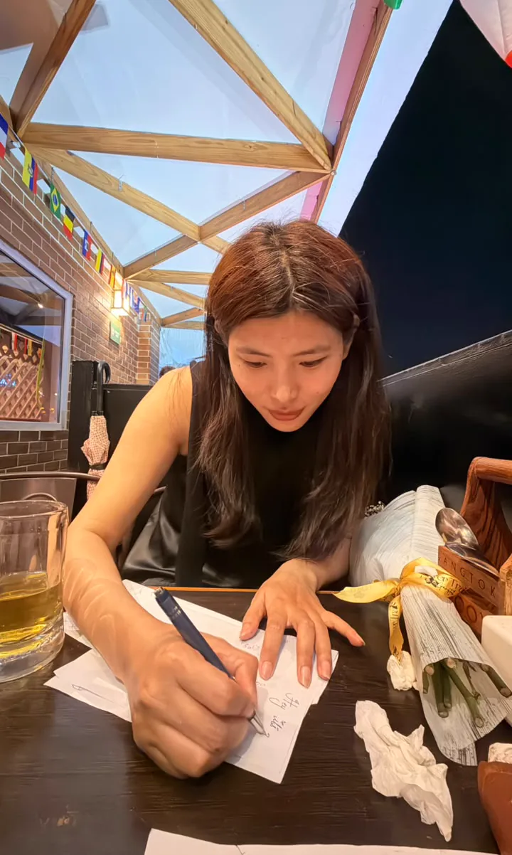 Sonam drawing at the table with papers and other items visible around her.