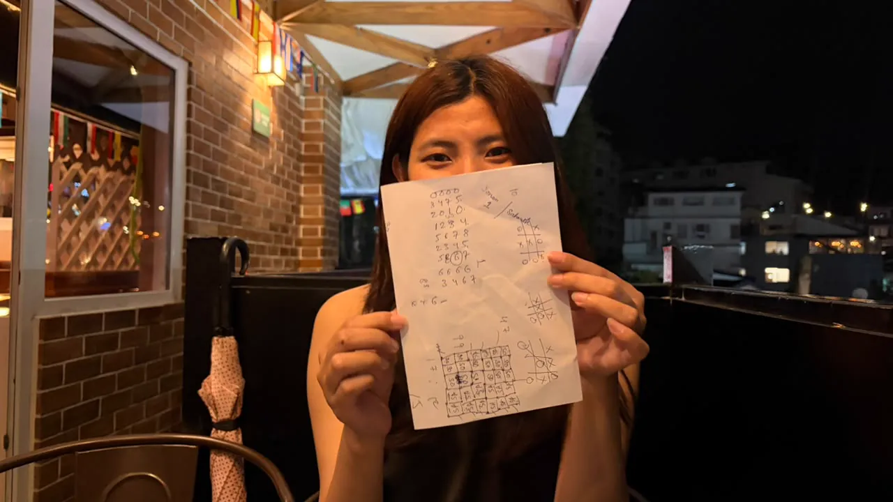 Sonam holding up a sheet covered with marks from a paper game.