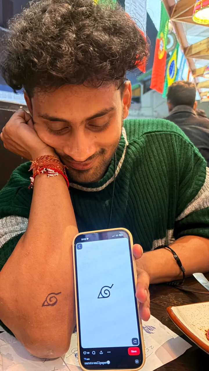 An arm with a temporary leaf-like drawing beside a phone reference while Saharsh looks on.