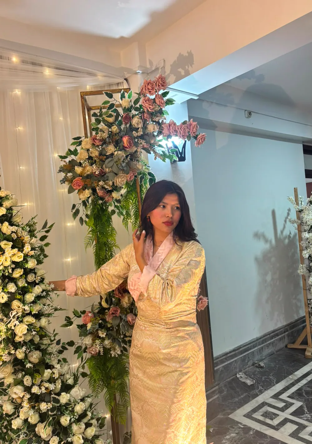 Sonam dressed in a light-colored outfit at an indoor event with flowers behind her.