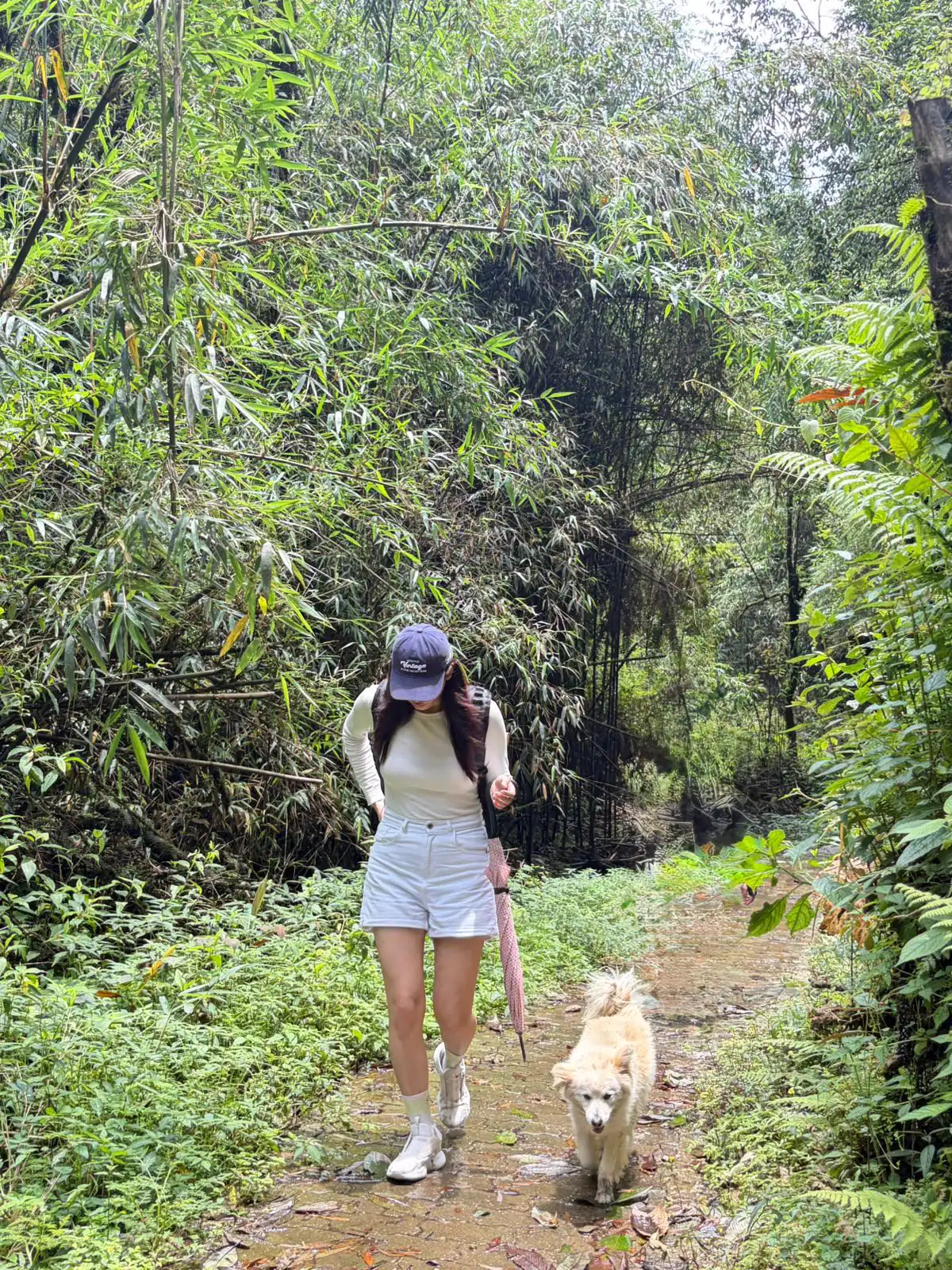 Sonam walking along a green forest path beside a dog.
