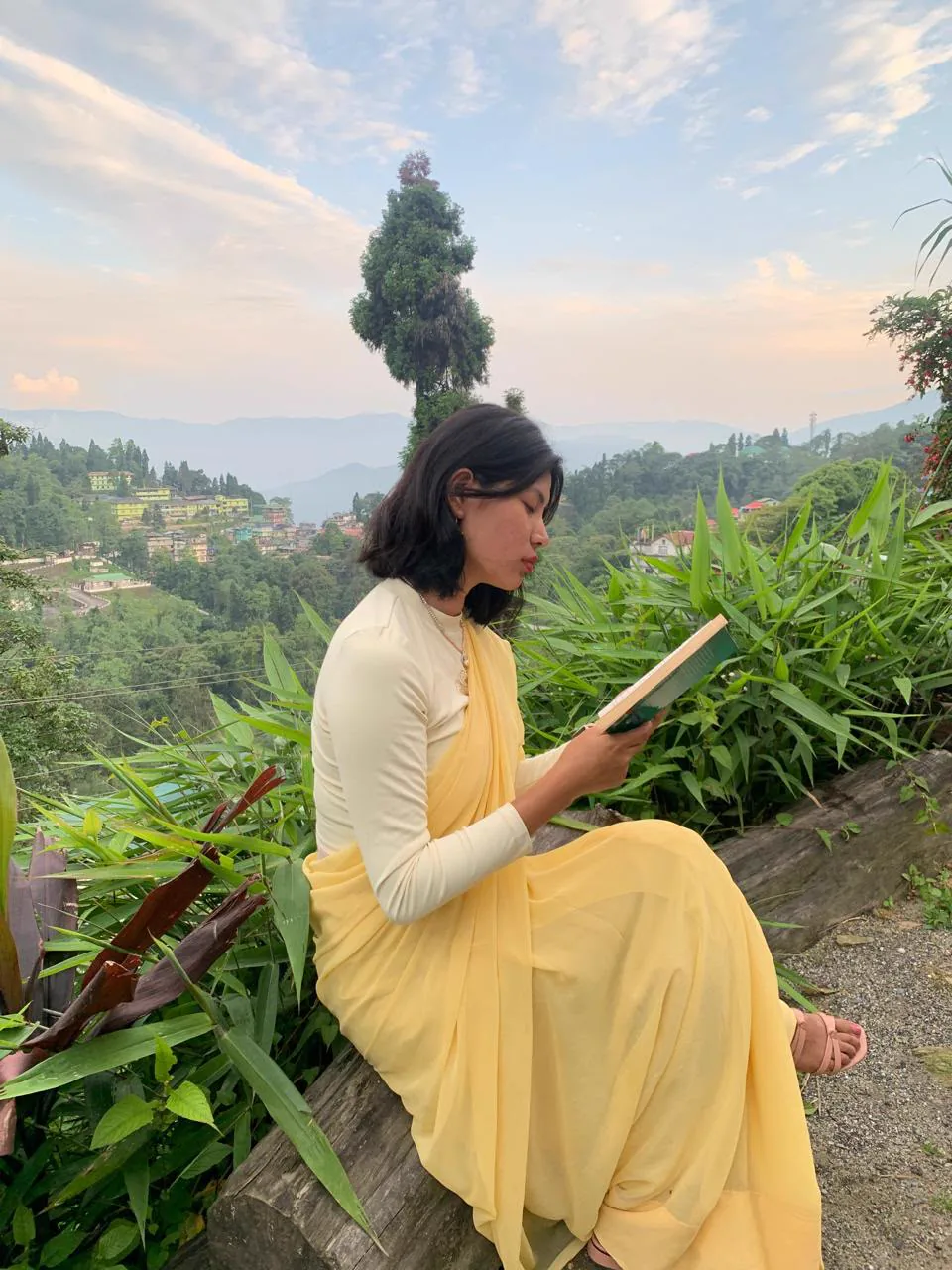 Sonam sitting outdoors in the hills while reading a book.